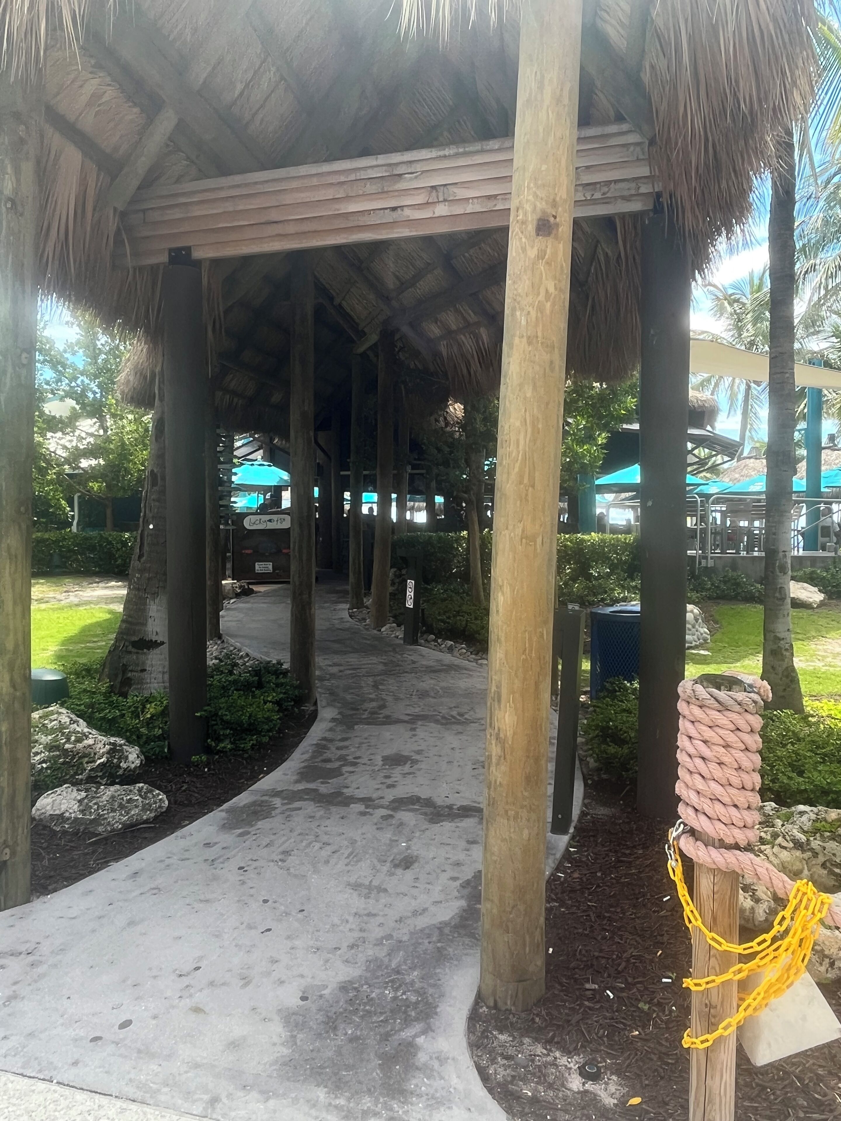 A covered walkway with wooden pillars, a concrete path, and a rope swing.