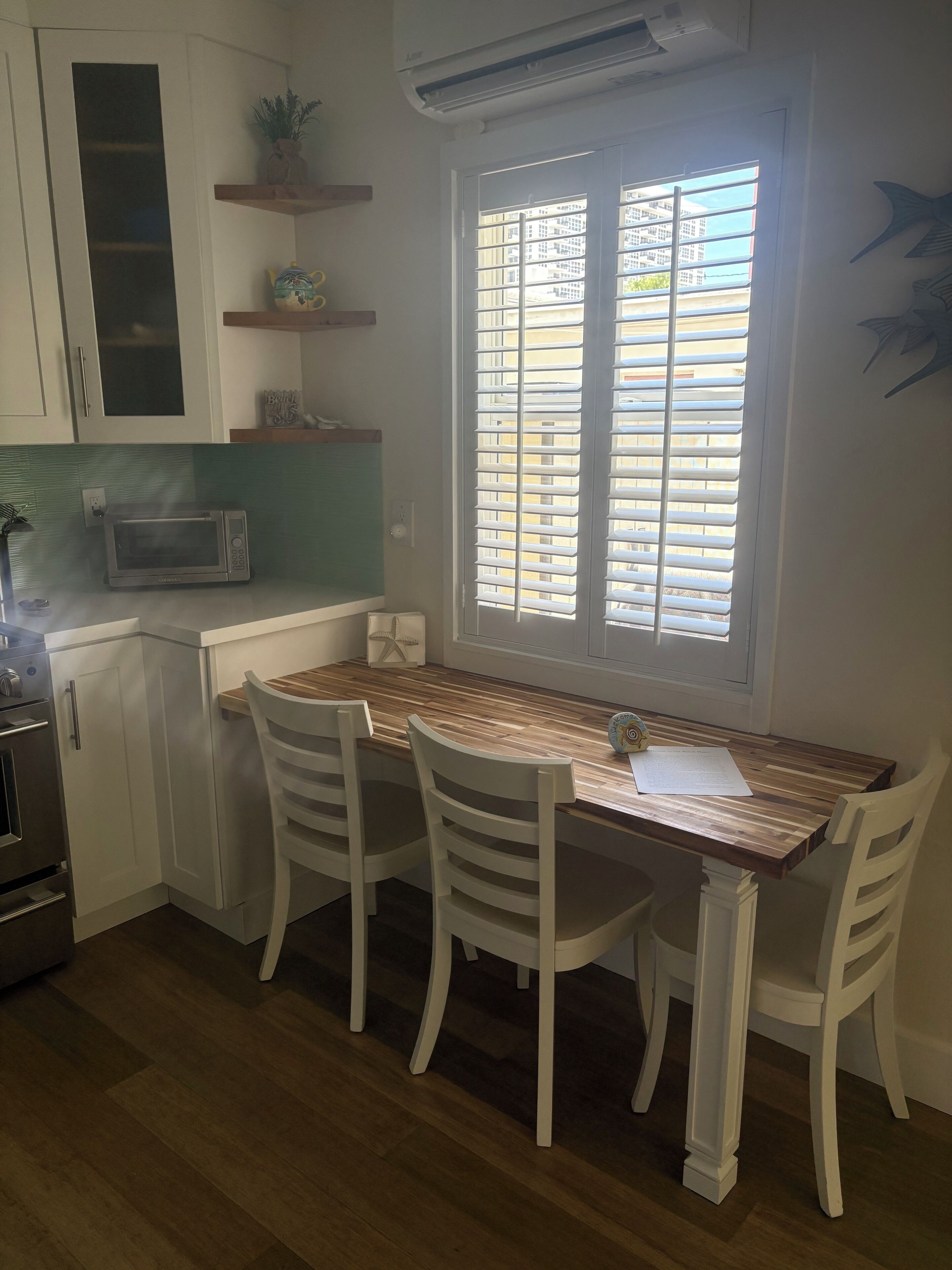 A kitchen with white cabinets, a microwave, a window with blinds, and a dining table with chairs.