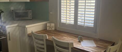 A kitchen with white cabinets, a microwave, a window with blinds, and a dining table with chairs.