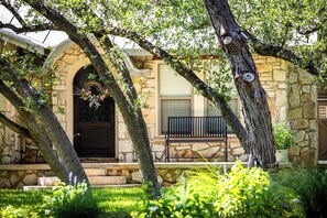 Set amidst lush greenery, this traditional building features a stone archway entrance and a cozy porch with a bench.