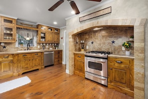 Kitchen with wooden cabinetry, stainless steel range, oven, and stone backsplash.