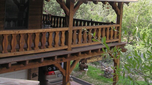 Ein Holzbau mit geneigtem Dach, einem Balkon mit Geländer und Blick auf eine gebirgige Landschaft.