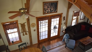 Ein gemütliches Wohnzimmer mit Deckenventilator aus Holz, einem großen Fenster mit Aussicht, einem dunkelgrauen Sofa und einem kleinen Tisch.