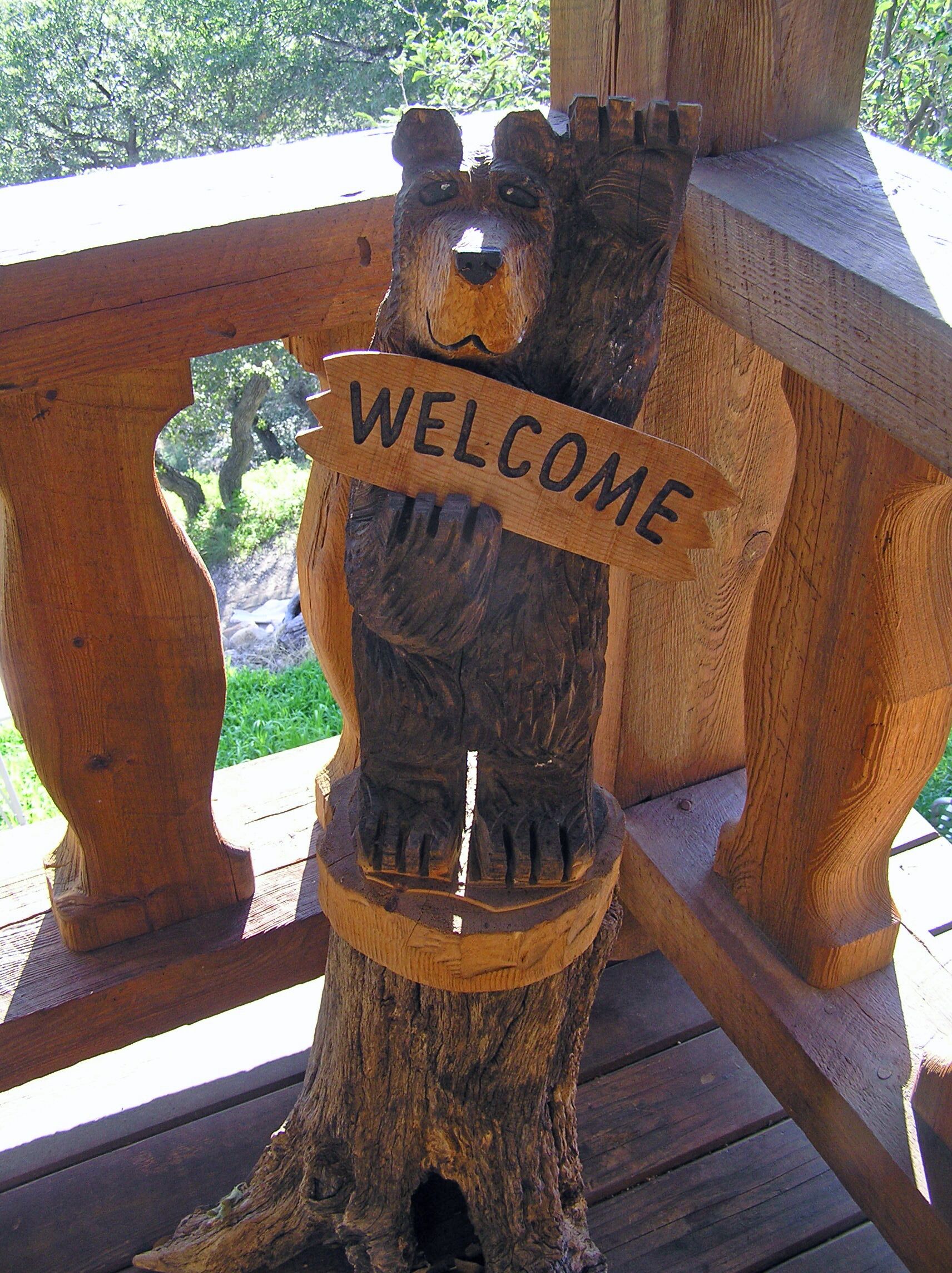 A wooden bear sculpture with a 'WELCOME' sign on a wooden deck.