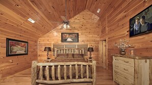 Un dormitorio de cabaña de troncos con cama, cómoda y ventilador de techo.