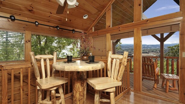 Una terraza de madera con una mesa redonda y cuatro sillas, con vista a un paisaje pintoresco.