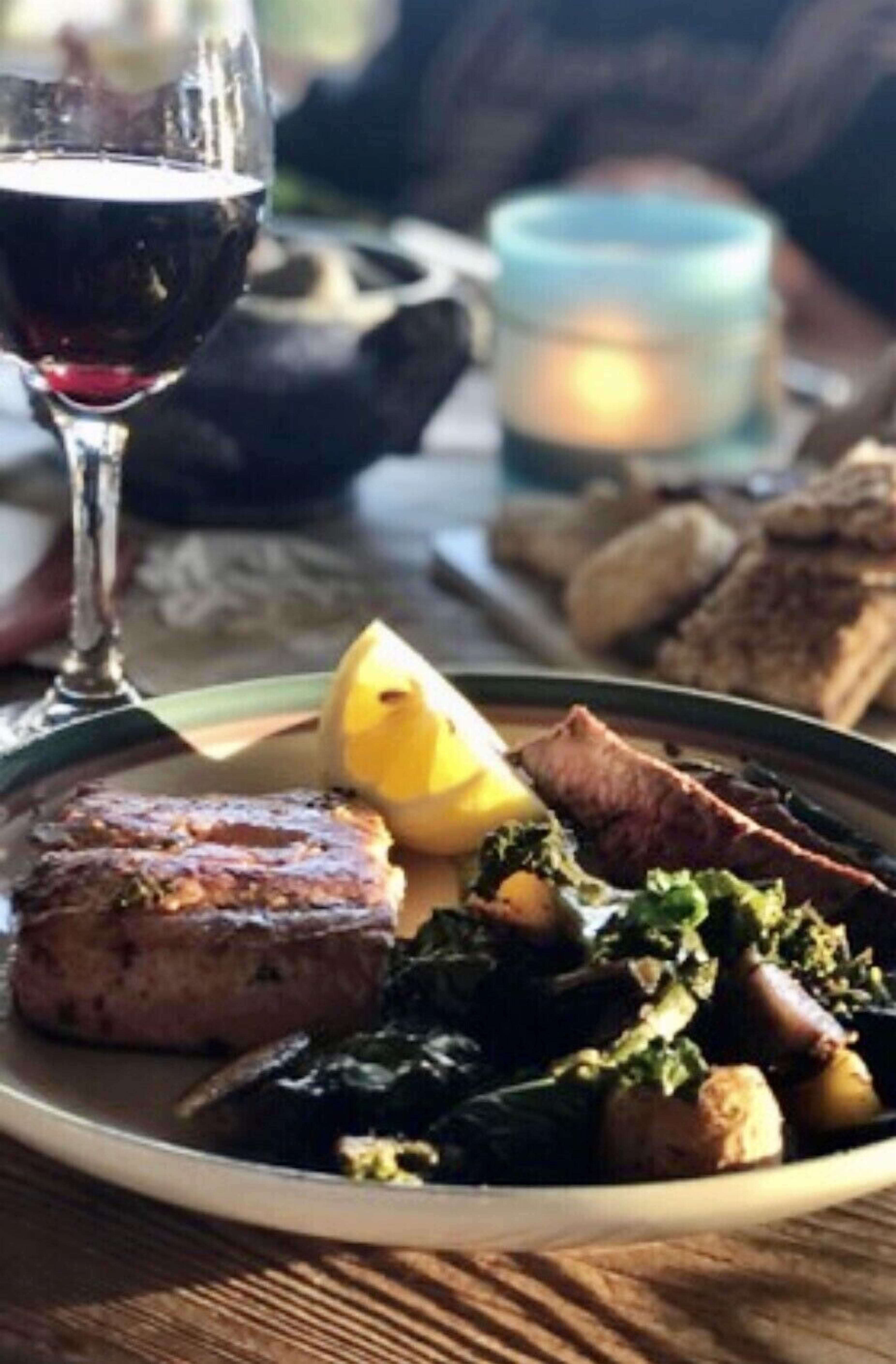 A plate of food with a glass of red wine, a candle, and bread on a table.