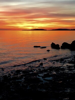 Ein Sonnenuntergang über einem ruhigen Meer mit felsiger Küste.