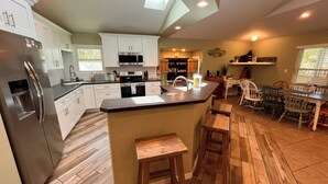 Een moderne keuken met witte kastjes, een roestvrijstalen koelkast, een centraal eiland met krukken, en een eethoek met een houten tafel en stoelen.