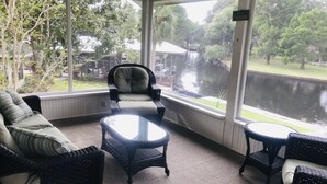 Een zonnedoorspoelde kamer met rieten meubels, grote ramen en uitzicht op een wateroppervlak.