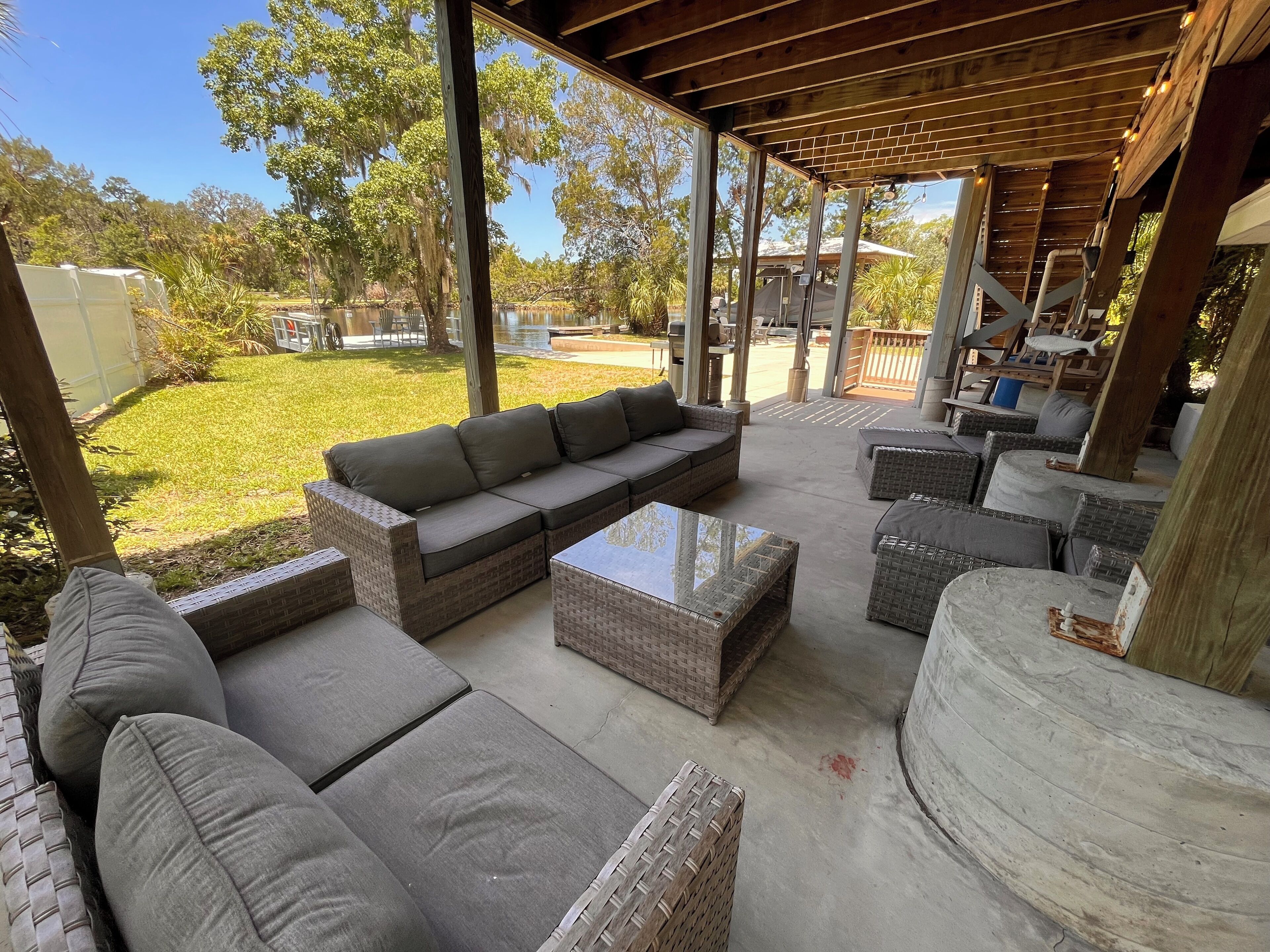 A covered outdoor patio with wicker furniture, including a sofa and ottomans, and a glass coffee table.