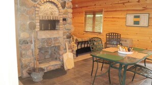 Una chimenea de piedra con estufa de leña, una mesa de comedor con sillas y una ventana con persianas.