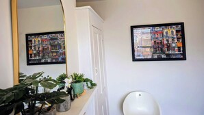 A bathroom with a large mirror, two framed artworks, a toilet, and a plant arrangement. - Luxury 4/5 bed 2 bath Victorian London home (London)