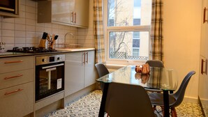 A compact kitchen with a gas stove, oven, and a dining table with chairs. - Luxury 4/5 bed 2 bath Victorian London home (London)