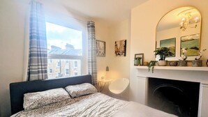 A bedroom with a bed, a fireplace, a mirror, and a window with curtains. - Luxury 4/5 bed 2 bath Victorian London home (London)