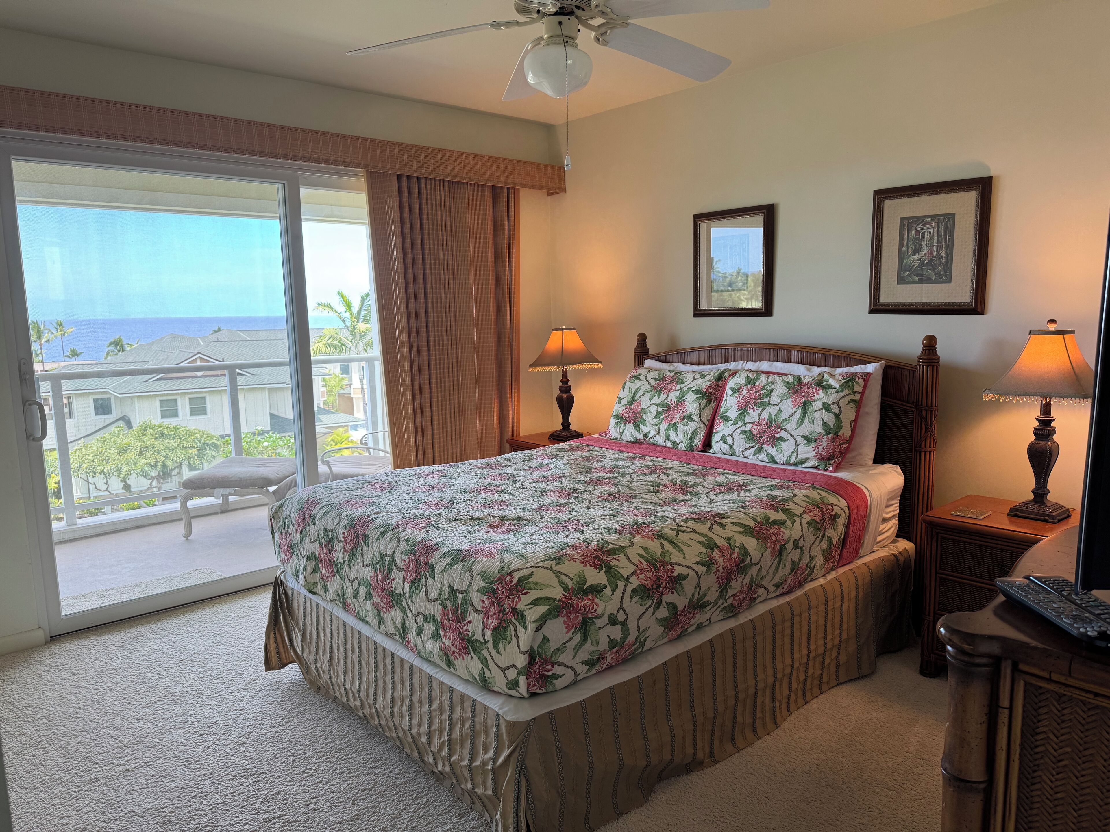A hotel room with a large bed, two bedside lamps, a ceiling fan, and a view of the ocean through a sliding door.