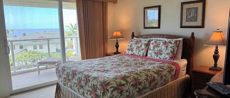 A hotel room with a large bed, two bedside lamps, a ceiling fan, and a view of the ocean through a sliding door.