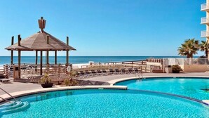 A pool area with a gazebo, lounge chairs, and a view of the ocean.