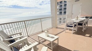 A balcony with white furniture, including chairs and a table, overlooking a beach.