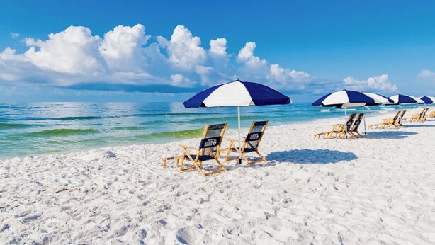 A beach with white sand and clear blue water. There are several beach chairs and umbrellas.