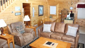 A wooden cabin interior with a sofa, armchairs, a dining table, a kitchen area, and a staircase. - The Cabin at Eagle Feather - Hot Tub, Pool Table! Seasonal Pool Mountain View (Sevierville)
