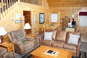 L’intérieur d’un chalet en bois comprend un canapé, des fauteuils, une table à manger, un coin cuisine et un escalier.