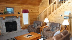A wooden interior with a stone fireplace, leather sofas, a wooden coffee table, and a staircase. - The Cabin at Eagle Feather - Hot Tub, Pool Table! Seasonal Pool Mountain View (Sevierville)