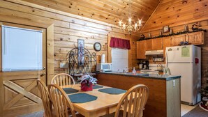 A wooden cabin interior with a dining area, kitchen, and a chandelier. - The Cabin at Eagle Feather - Hot Tub, Pool Table! Seasonal Pool Mountain View (Sevierville)