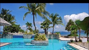 A pool area with palm trees and a view of the ocean. - "THREE PALMS"~ON beach, remodeled, private patio, generator, pool, quiet & clean (St. Thomas)