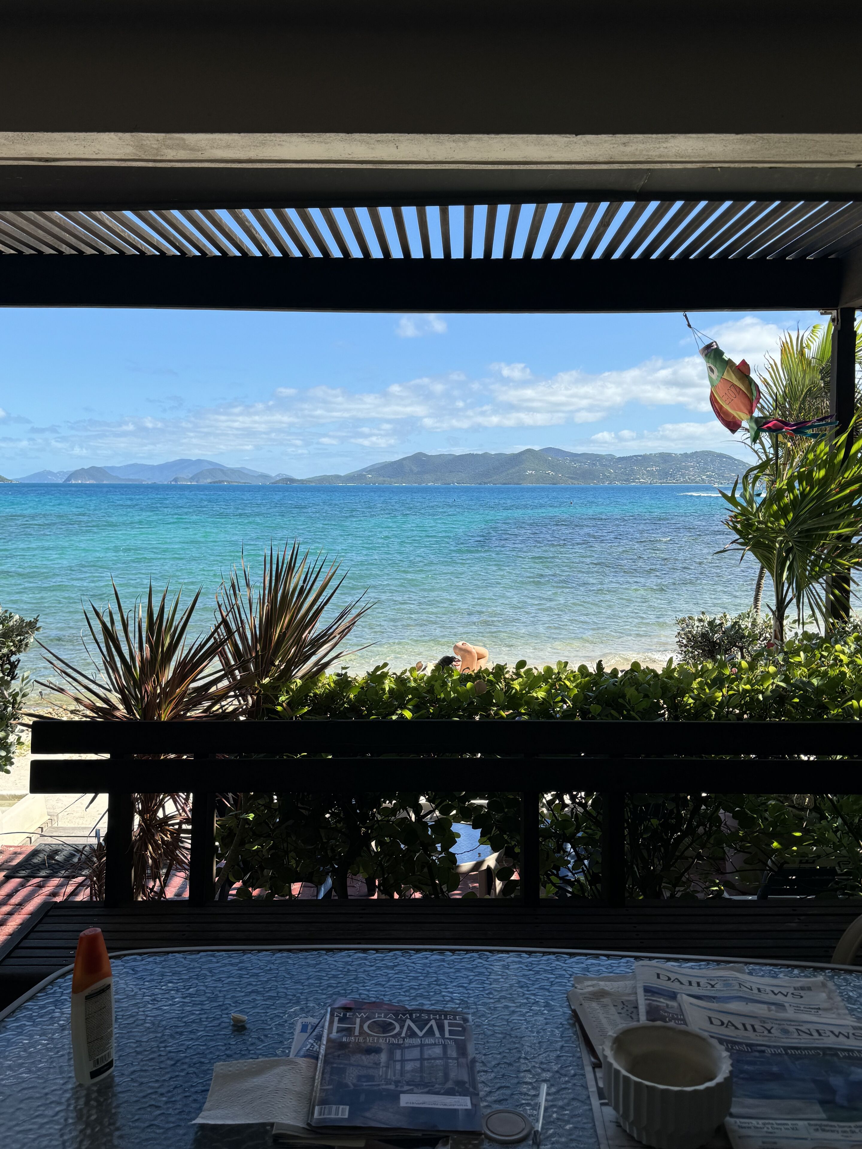 A view from a balcony overlooking a beach with clear blue water and distant mountains.