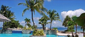 A pool area with palm trees and a view of the ocean. - "THREE PALMS"~ON beach, remodeled, private patio, generator, pool, quiet & clean (St. Thomas)