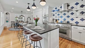A modern kitchen with white cabinets, a central island with stools, stainless steel appliances, and pendant lighting. - Second Wind :039-O  An Orleans Estate with large heated pool, spa, on Town Cove; sleeps 24 (Orleans)