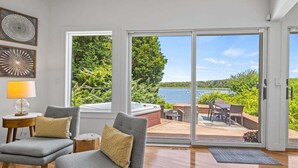 A modern living room with a large sliding glass door leading to an outdoor deck with a view of a lake. - Second Wind :039-O  An Orleans Estate with large heated pool, spa, on Town Cove; sleeps 24 (Orleans)