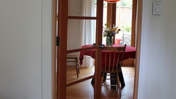 Corridoio che conduce a una sala da pranzo, con una porta in legno, un tavolo con tovaglia rossa e un lampadario arancione.