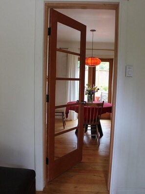 A hallway leading to a dining area with a wooden door, a table with a red tablecloth, and a hanging orange light fixture.