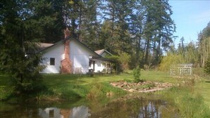 Una casa bianca con un camino, circondata da uno stagno e alberi.