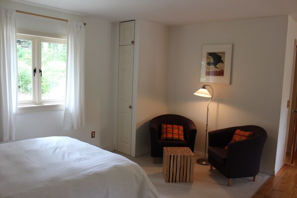 A bedroom with a bed, a chair, a floor lamp, and a door.