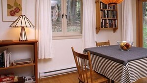 Zona pranzo con tavolo, sedie, lampada, libreria e finestra con tende.