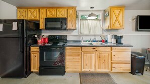 A kitchen with wooden cabinets, a black refrigerator, a microwave, an oven, and a sink. - Pool Side Guest House On Lake Hudson Near Pryor (Adair)