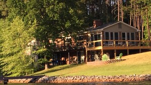 A lakeside lodge with a large deck, a stone retaining wall, and a grassy area. - Flat Lot, Views! Waterslide, Firepit, Kayaks, Pickleball, Pingpong, Tennis, WiFi (Moneta)