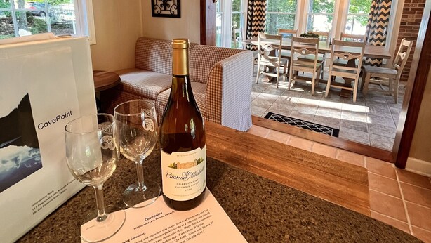 A wine bottle and glasses on a counter with a menu, a framed picture, and a view of a dining area with a chandelier. - Flat Lot, Views! Waterslide, Firepit, Kayaks, Pickleball, Pingpong, Tennis, WiFi (Moneta)