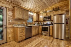 Enjoy cooking in this well-equipped kitchen with a refrigerator, oven, and microwave, surrounded by wooden paneling and a granite countertop.