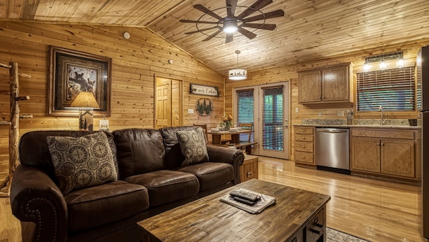 Interior acogedor de una cabaña con techo de madera, un sofá de cuero, una mesa de comedor y una zona de cocina.