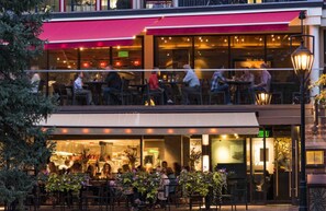 Ein Restaurant mit Außenbereich, einer roten Markise und einer Glasfassade.