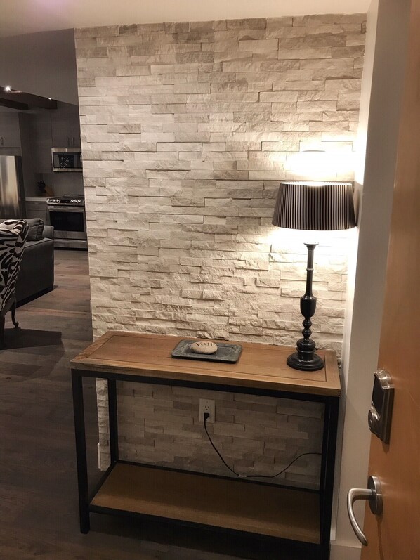 Ein modernes Wohnzimmer mit einer Wand im Steinoptik, einem Holztisch mit einer Dekoration und einer schwarzen Lampe.