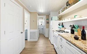 A narrow kitchen with white cabinets, a gas stove, and a countertop with kitchenware.