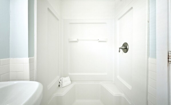 A white bathroom with a bathtub, a towel, and a door with a silver handle.