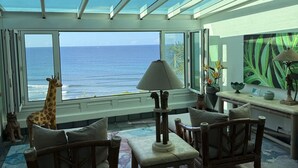 Habitación con un amplio ventanal con vista al océano, una estatua de jirafa, muebles de madera y un diseño de pared inspirado en la temática tropical.