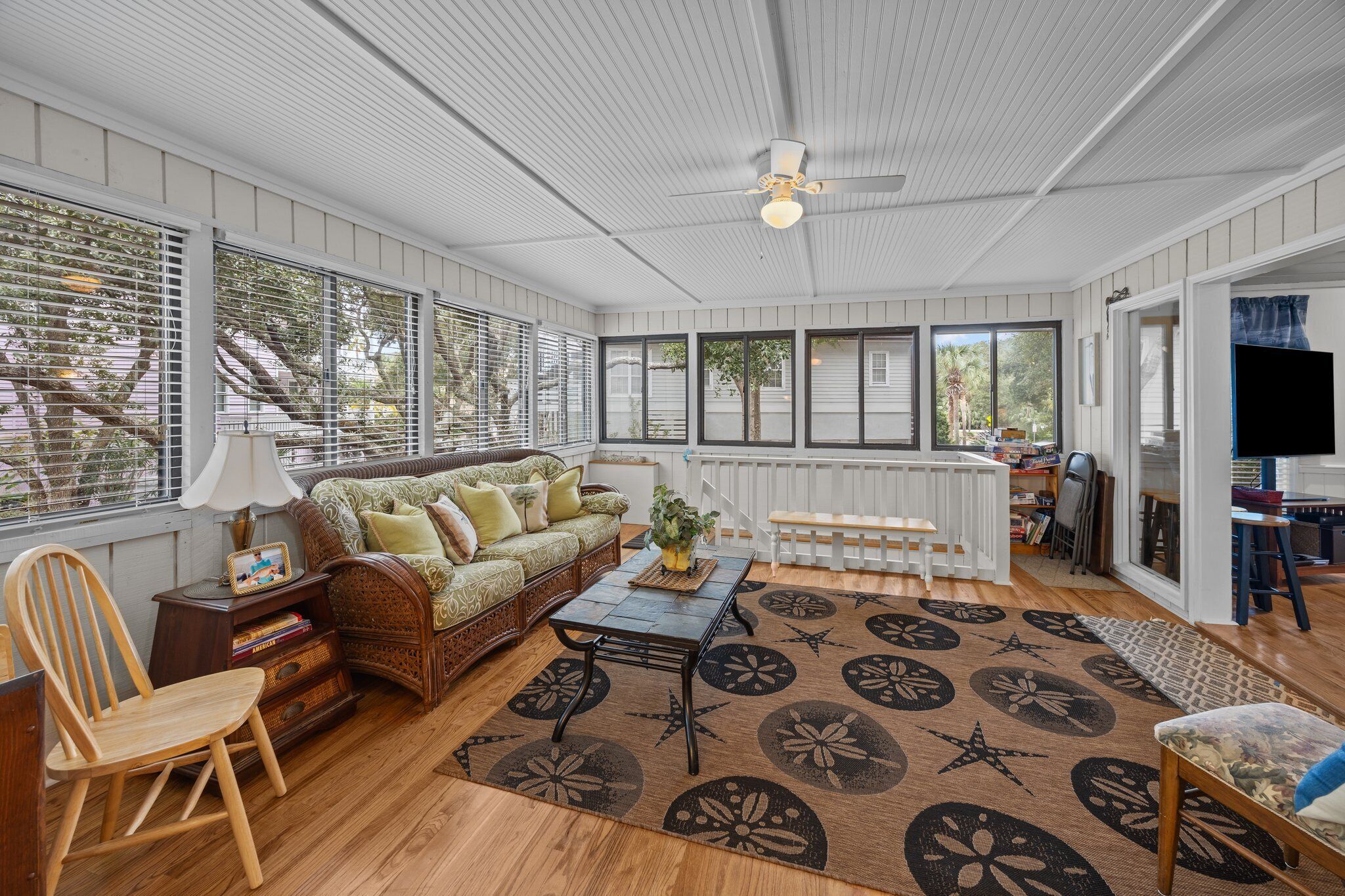 A spacious living room with a wooden floor, a green patterned sofa, a coffee table, and a ceiling fan.
