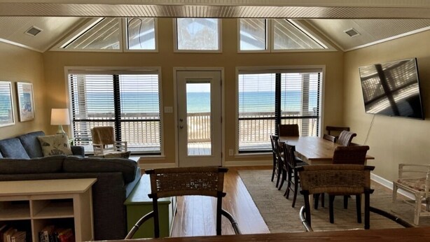 Amplia sala de estar con un gran ventanal con vista a la playa, una mesa de comedor con sillas y un sofá.